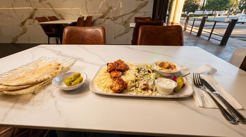 Chicken shish tawook plate with rice, salad, hummus, and pita bread on a marble table.