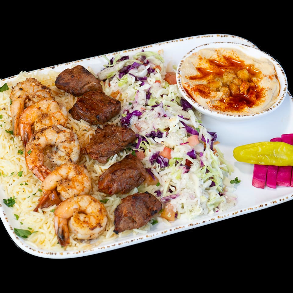 A platter with grilled shrimp, beef chunks, rice, coleslaw, hummus, and pickled vegetables.