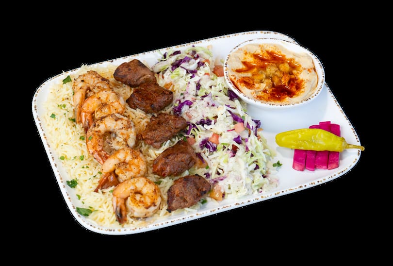 A platter with grilled shrimp, beef chunks, rice, coleslaw, hummus, and pickled vegetables.