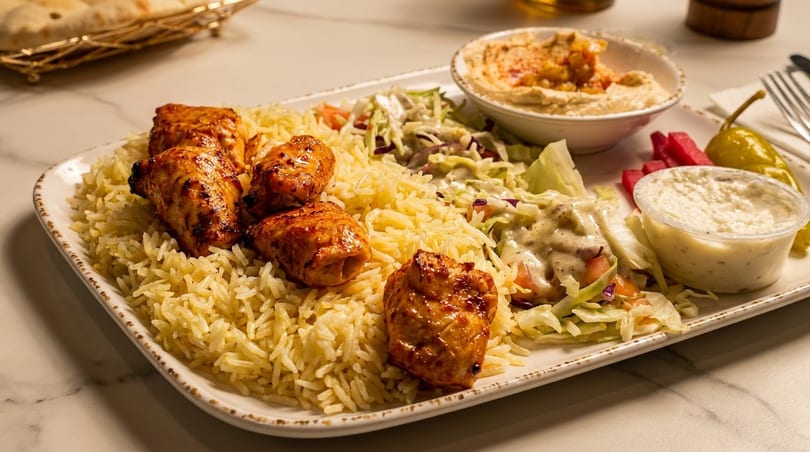 Chicken and rice platter with salad, hummus, and sauces on a white plate.