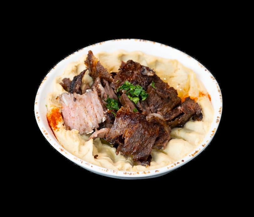 A bowl of creamy hummus topped with savory shredded meat, fresh parsley, and a sprinkle of paprika.