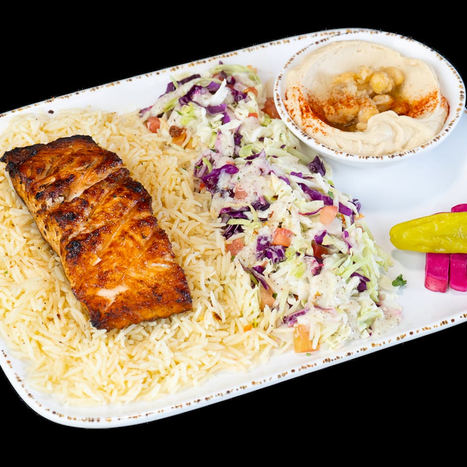 Grilled salmon with rice, coleslaw, hummus, and pickled vegetables on a white plate.
