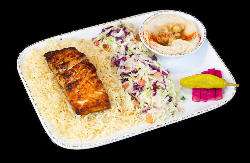 Grilled salmon with rice, coleslaw, hummus, and pickled vegetables on a white plate.