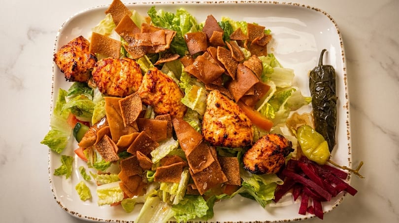 Grilled chicken pieces on a bed of fresh lettuce, topped with crispy pita bread, pickled peppers, and beets.
