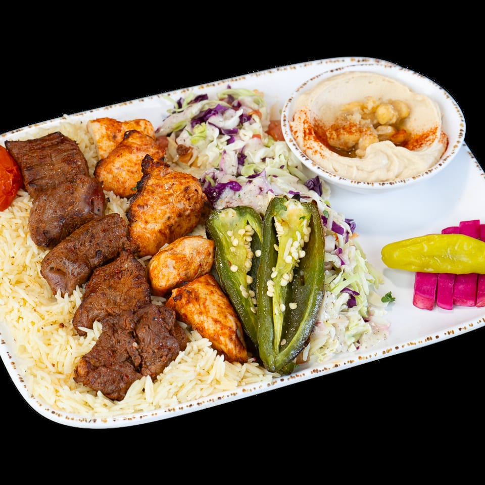 A platter with rice, beef and chicken kebabs, coleslaw, hummus, grilled peppers, and pickled vegetables.