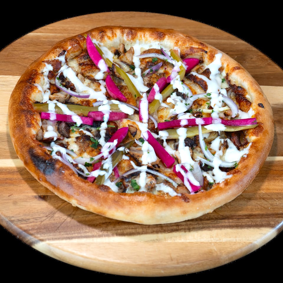 Shawarma pizza with chicken, red onions, pickles, and white sauce on a wooden board.