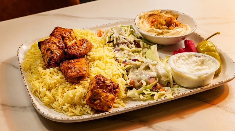 A platter of chicken shish tawook with yellow rice, salad, hummus, and tzatziki sauce.