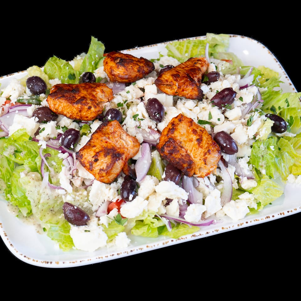 Grilled chicken salad with lettuce, feta, olives, red onion, and dressing on a white platter.