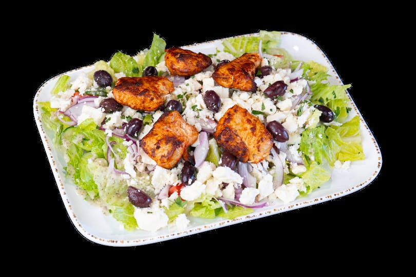 Grilled chicken salad with lettuce, feta, olives, red onion, and dressing on a white platter.